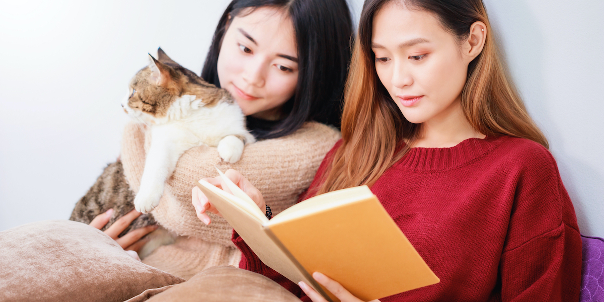 two women reading from the same book, with a cat