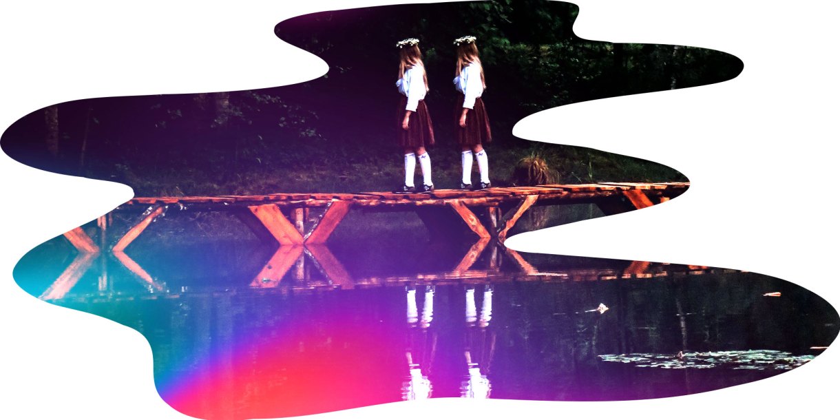 two girls in school uniforms walking across a bridge over the water in a forest