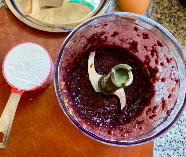 the bottom half of a mini food processor, the S-shaped blade, with blended blackberries and miso as a paste. a little 1/3 cup of flour sites beside the food processor.