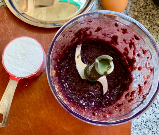 the bottom half of a mini food processor, the S-shaped blade, with blended blackberries and miso as a paste. a little 1/3 cup of flour sites beside the food processor.