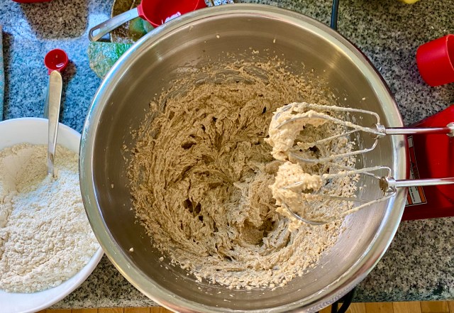 overhead shot of a mixing bowl with a creamy mixture of butter, sugar and eggs, hanging on the end of of the mixers