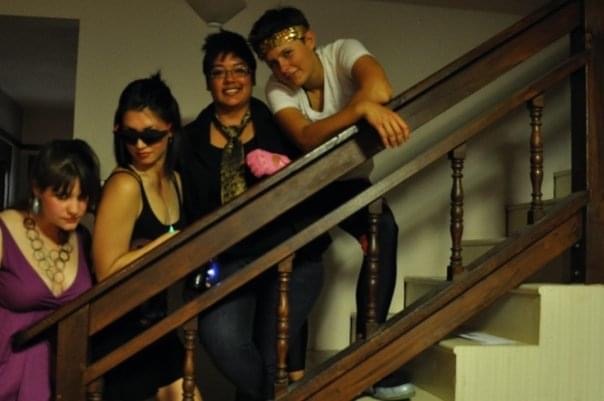 four women are lined up against a railing of staircase, preparing to go to a queer dance party.