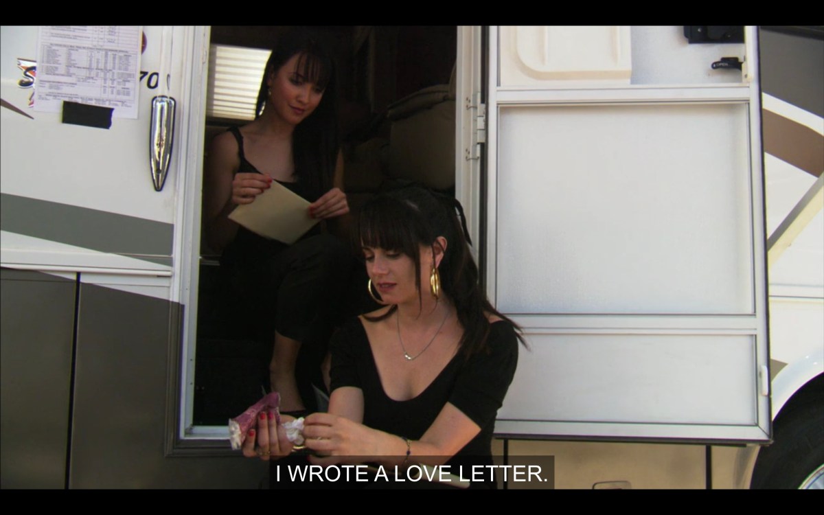 Jenny sitting outside of a Lez Girls trailer showing Adele a love letter she wrote