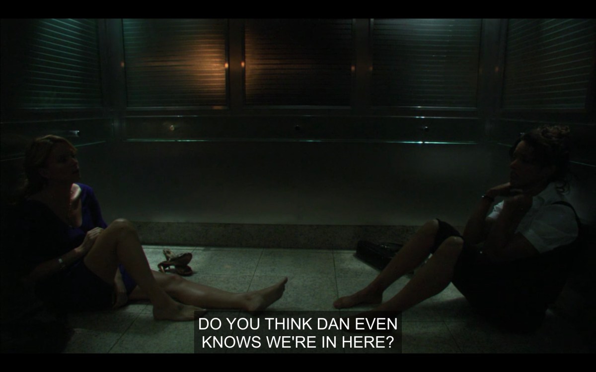 Tina and Bette sitting on the elevator floor with their shoes off