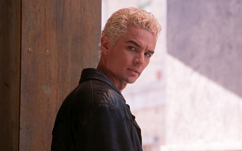 A bleach blonde man in a black leather jacket turns over his shoulder.