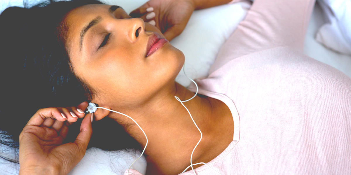 A South Asian woman in a pink sweater listens to music on her headphones, her mind at peace.