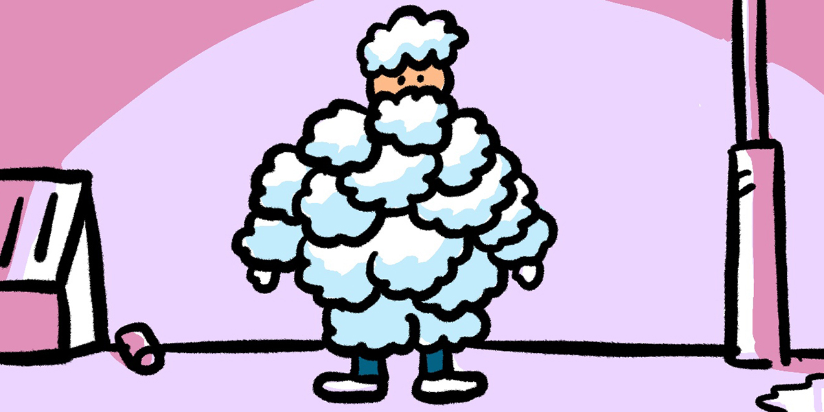 A person stands covered from head-to-toe in fluffy white balls, almost like snow, against a pink background.