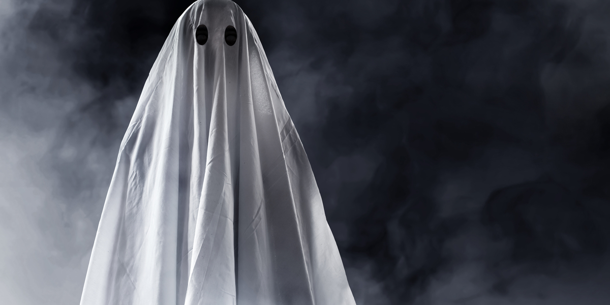 A white ghost floats in fog in front of a black background