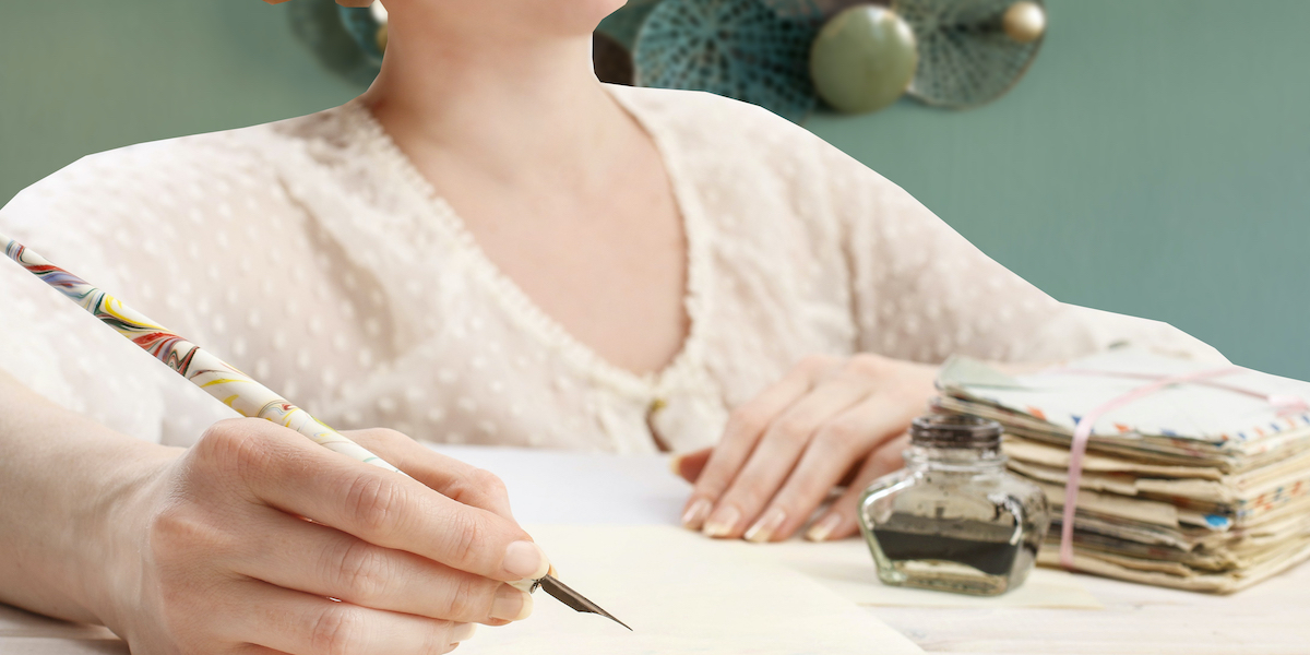 A woman in Victorian period dress sits writing a letter with a fountain pen