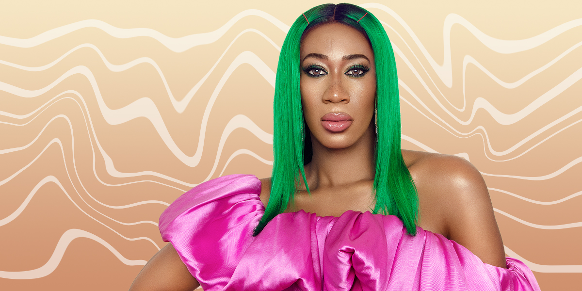 A portrait of Mila Jam wearing bright green center-parted hair with hot pink bobby pins and a pink taffeta one-shoulder top with a dramatic ruffle