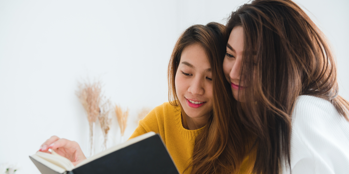 two Asian people with long hair leaning in together over an oversized book