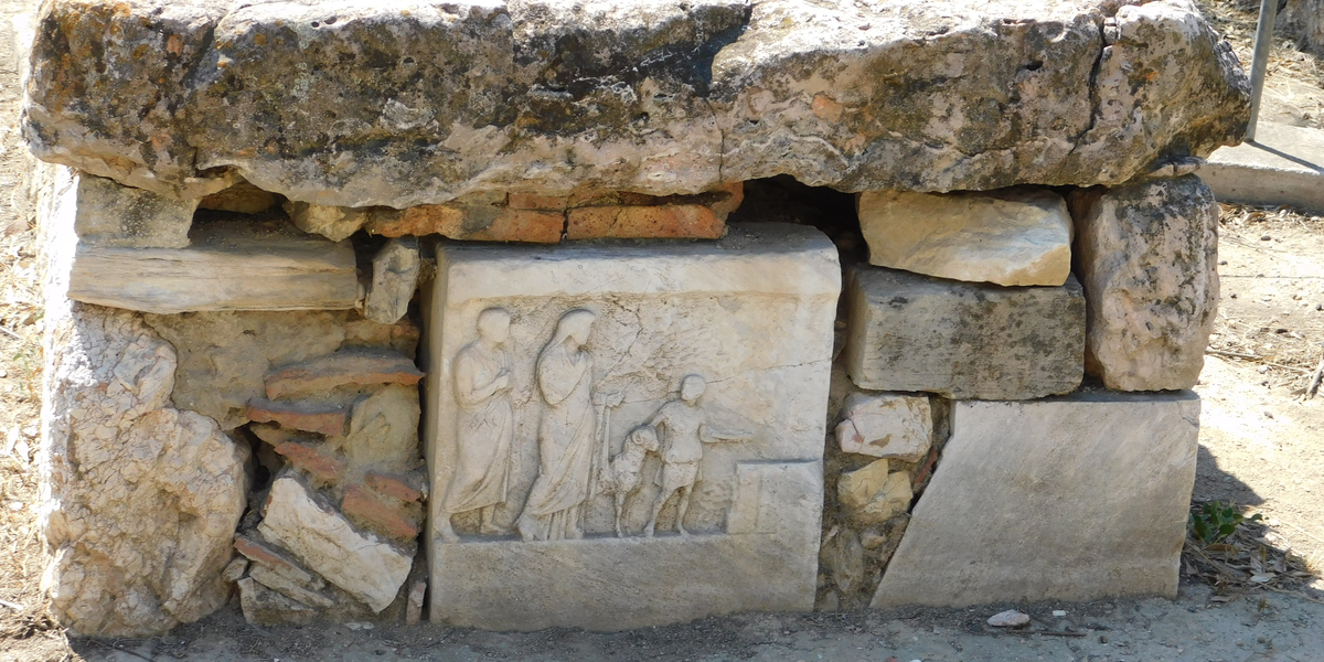 A ruined stone wall containing acarve dstone relief of several Greek figures