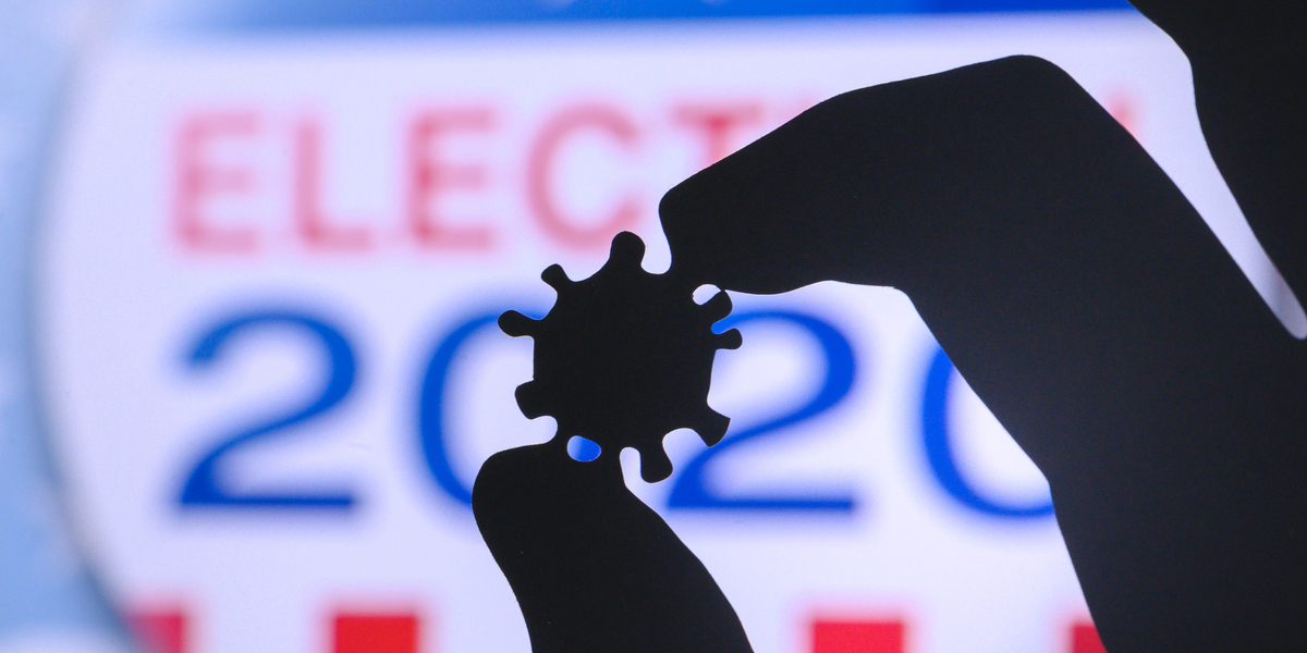 A close-up backlit hand holds a tiny model of a COVID-19 virus against a backdrop that reads ELECTION 2020.