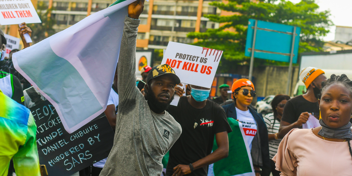 A photo of protesters in Nigeria with signs that read "Protect Us, Not Kill Us" and referring to ending SARS