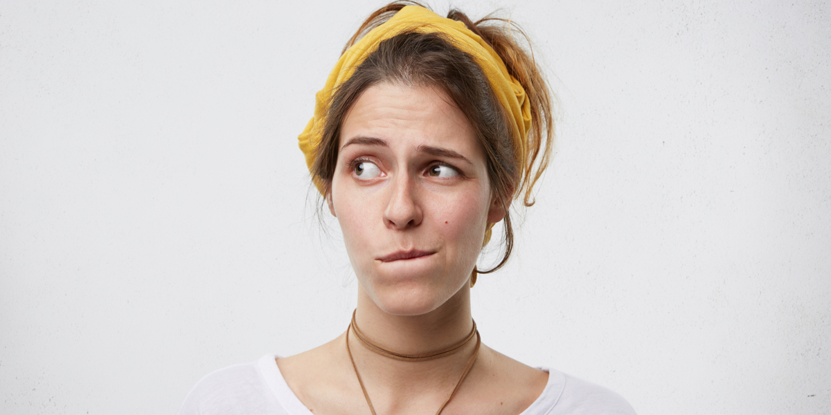 An unsure-looking white person with a scarf tied into their long hair and wearing a choker looks off to the side and bites their lip nervously