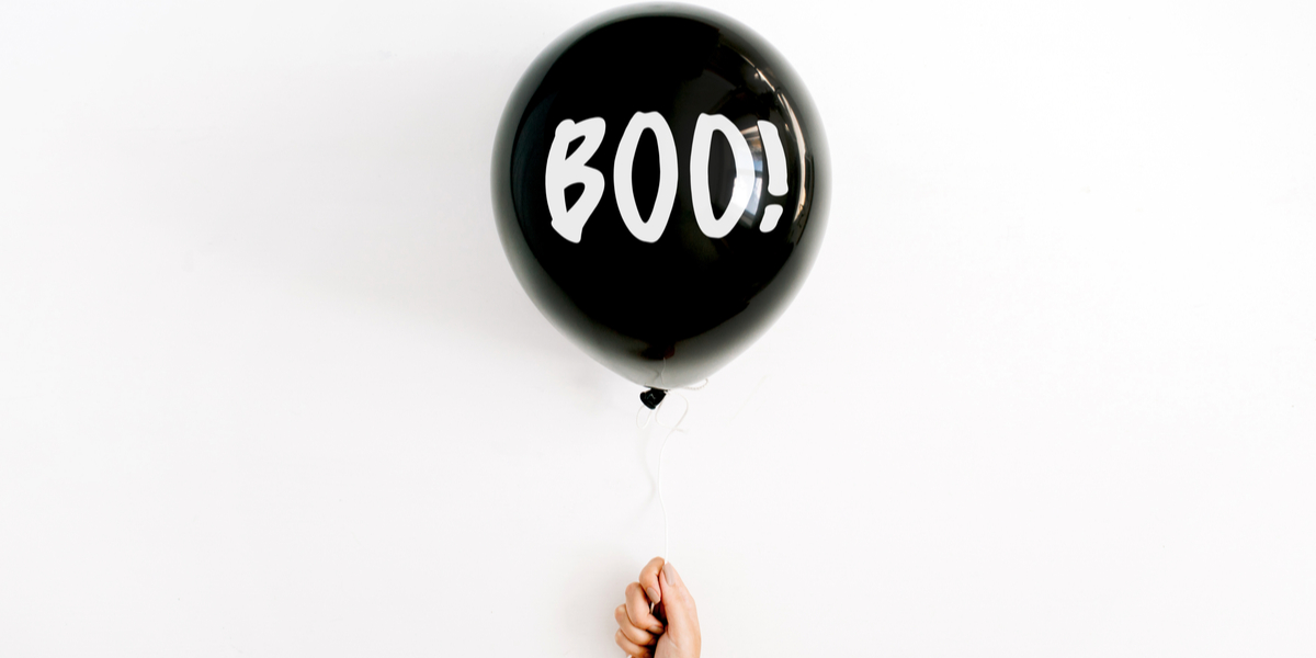 A disembodied hand holds up a floating balloon that reads BOO! against an empty white field
