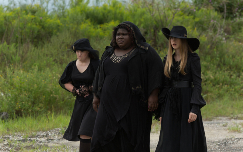 Three women in all black stand in front of trees.