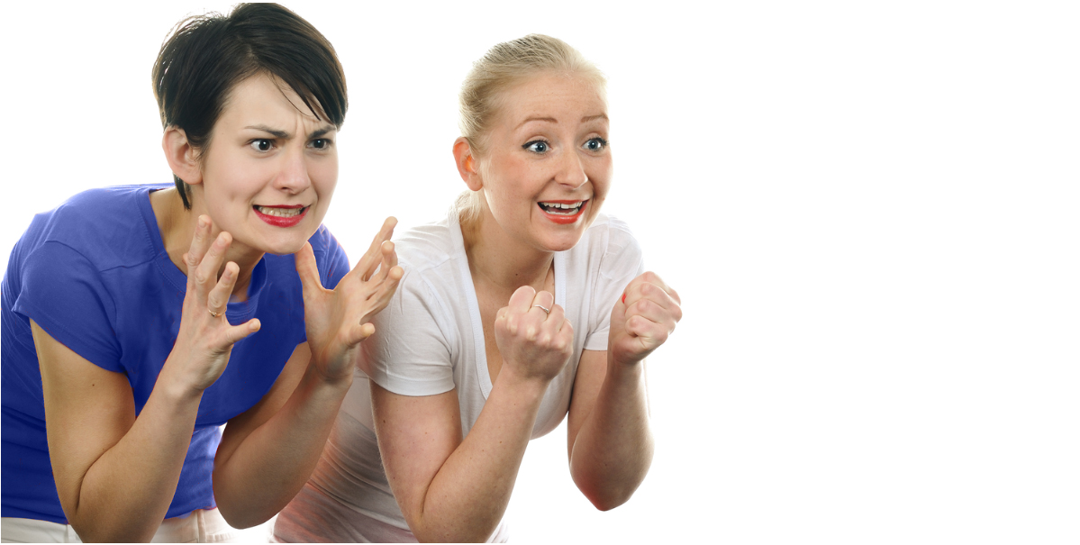 Two stressed-out-looking white women lean forward as if watching a basketball game intently, gesturing with their hands like they're upset by or excited about what's happening in the game, respectively