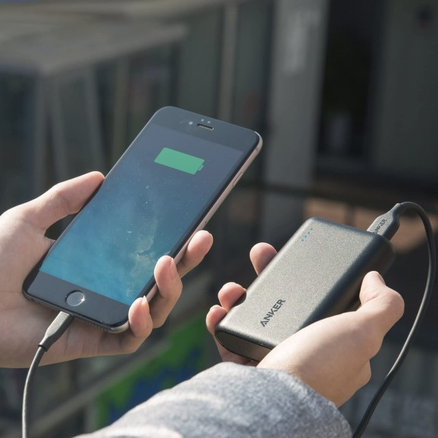 A person's hands are seen holding a phone connected to a portable charger