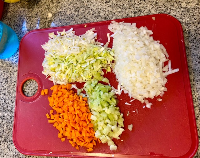 a read cutting board with piles of chopped carrots, leek, celery and onion