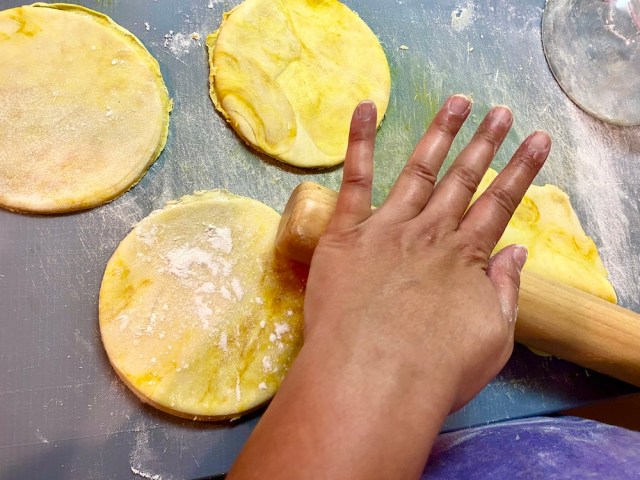 hands rolling out circles of yellow pie dough