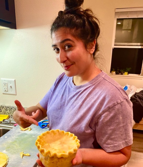 sarah in a purple t-shirt pointing to a well-crimped pie crust