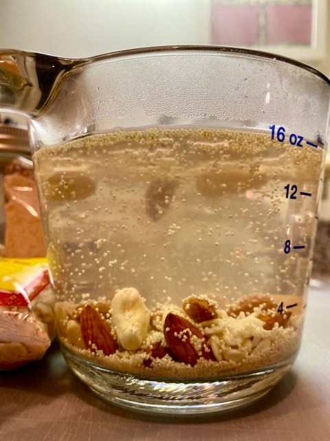 a glass measuring cup full of water with nuts and seeds floating in it