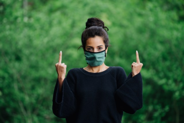 A woman in a green face masks holds up both middle fingers