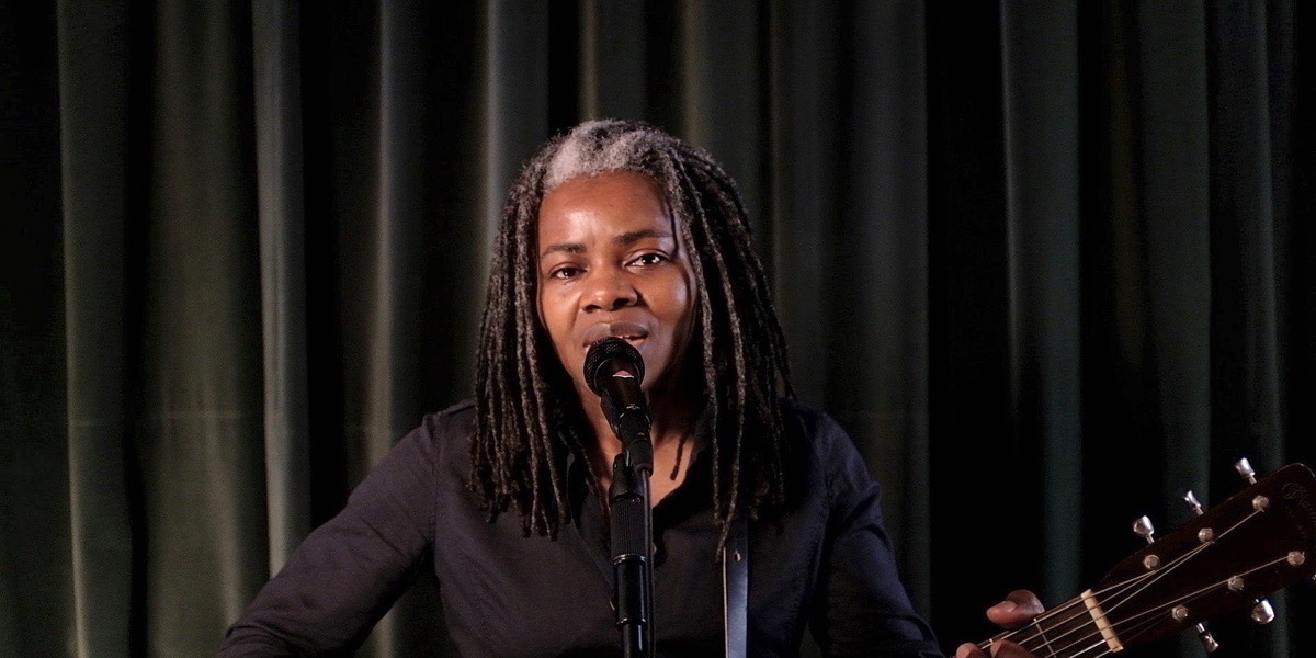 Tracy Chapmen on "Late Night With Seth Meyers." She is playing her guitar and wearing all black against a black background.