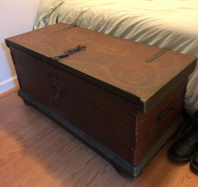 A dark wood hope chest style piece at the foot of a bed.