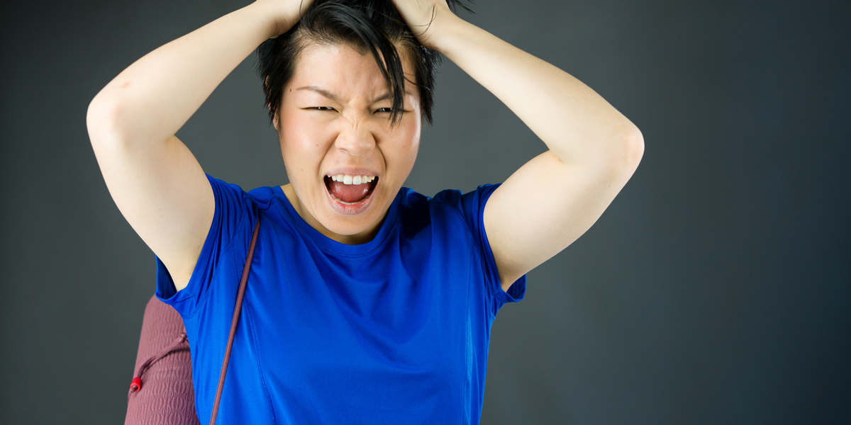 asian person grabbing their head out of frustration while carrying a yoga mat over one shoulder