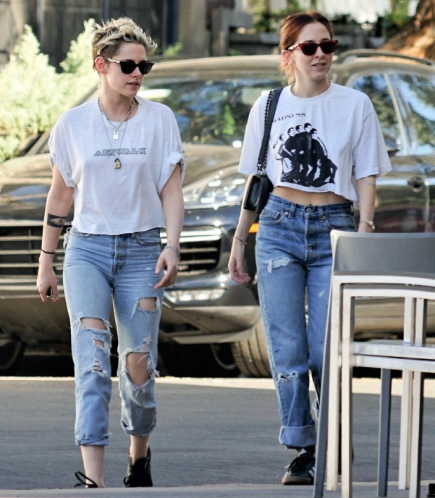 Kristen Stewart and Sara Dinkin walkng on the street, each wearing a white crop top, ripped jeans, sneakers and sunglasses.
