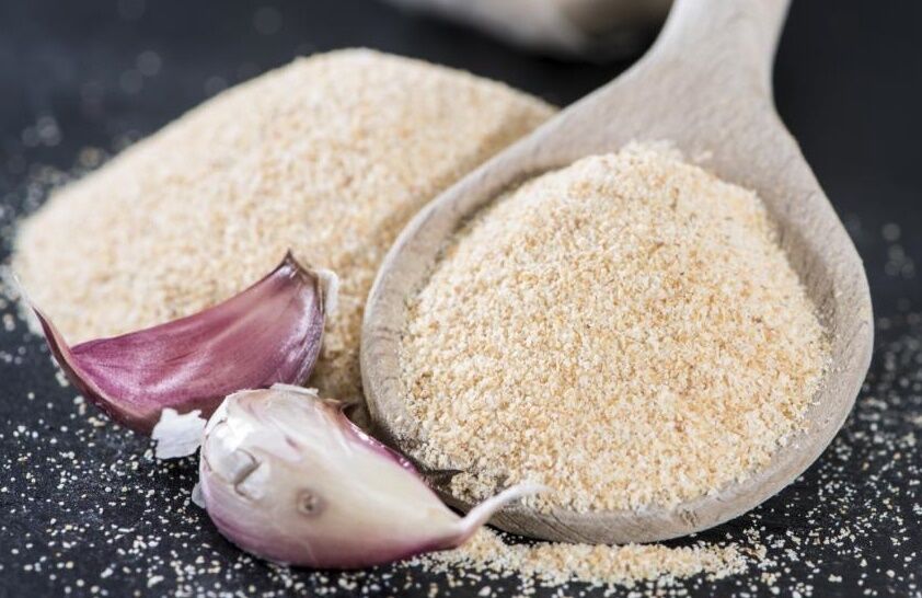 two unpeeled garlic cloves alongside a spoonful and small mound of garlic powder