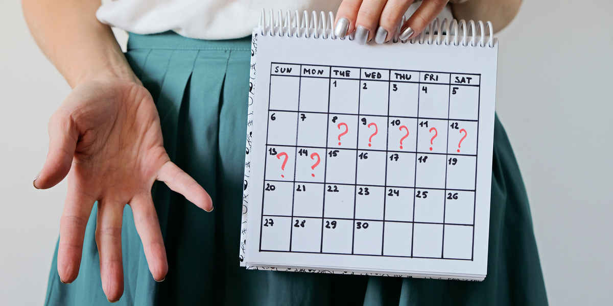 A person in a white shirt and green skirt holds up a calendar. Seven of the dates are marked with red question marks.