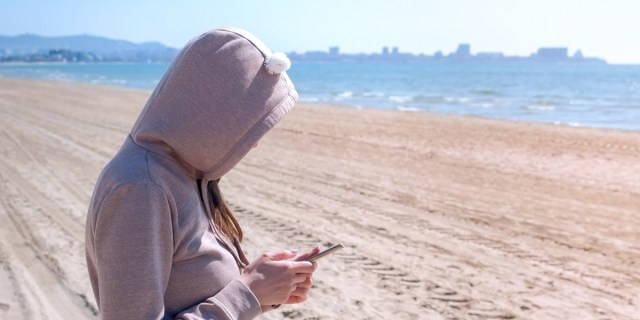 girl in hoodie on the beach reading a thing on her phone
