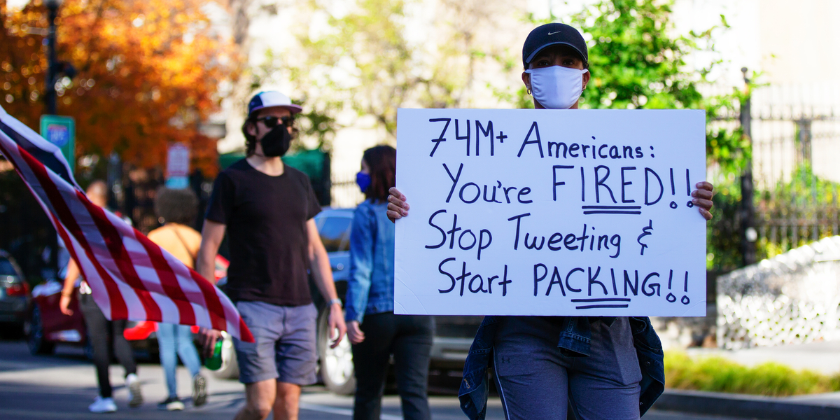 A masked person in a baseball cap holds up a sign that reads 74 million Americans: you're fired! Stop tweeting and start packing!