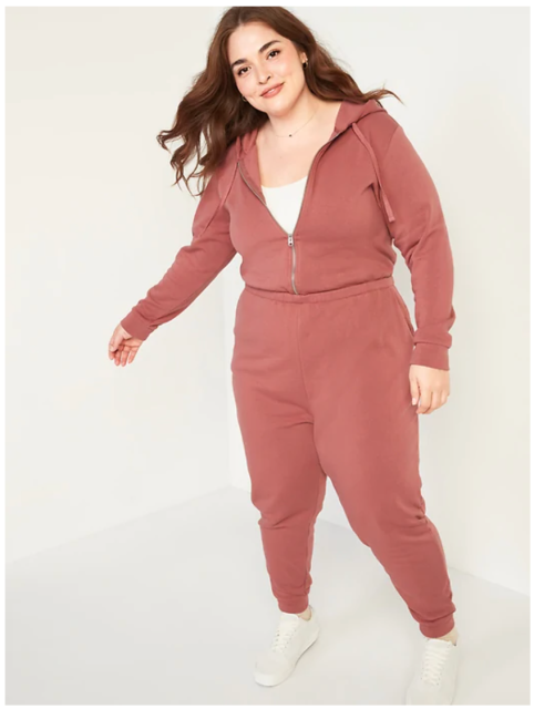 A smiling plus size model poses in a dusty rose zip up sweatsuit