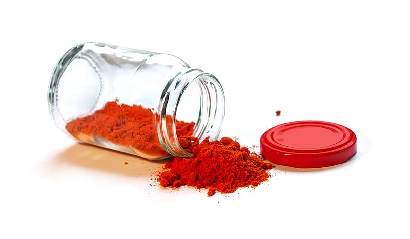 A clear glass jar full of bright red smoked paprika that has fallen on its side so the contents are spilling out