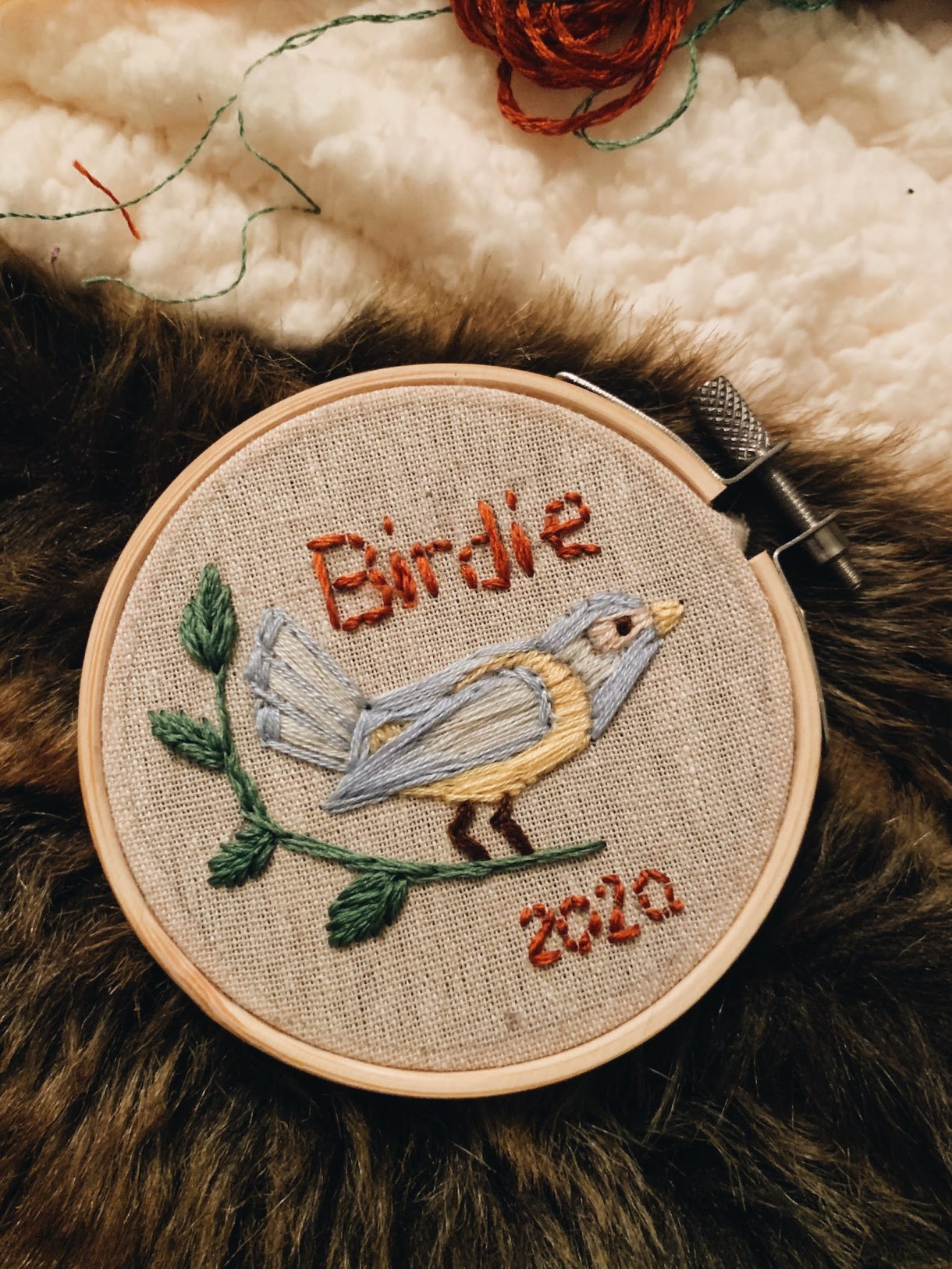 an embroidery ring with a small blue bird stitched on the fabric, the word Birdie in orange thread above the bird and the date 2020 stitched below