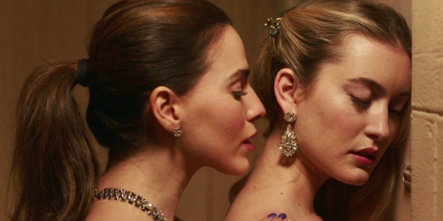In "Filthy Rich" Daisy, a woman with a brunette ponytail, kisses Becky, a blonde woman with her hair swept to the side, at the lower part of her neck. It's small and intimate.