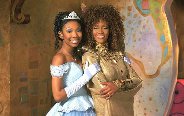 Still from Roger and Hammersteins 1997 "Cinderella". shows the two stars, Brandy and Whitney Houston, Brandy is wearing a pal blue ball gown and tiara and Whitney Houston is wearing a gold gown. 