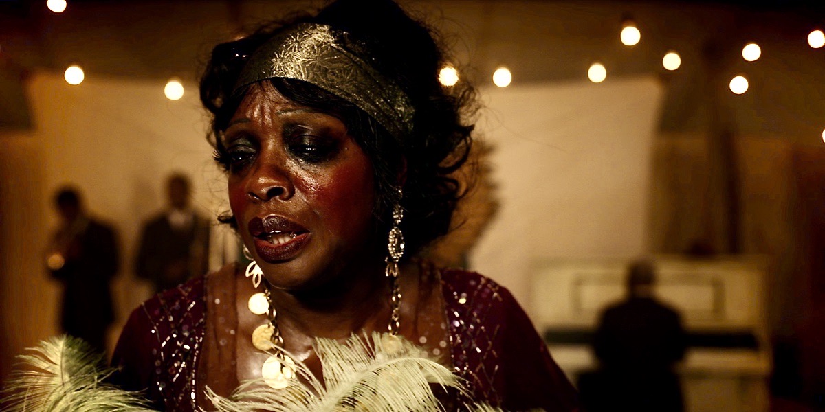 Viola Davis as Ma Rainey, in a gold headdress and a feather boa on stage. This is a still from Netflix's "Ma Rainey's Black Bottom" the latest entry into a queer history of the Blues legend.