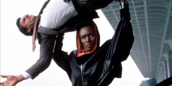 Grace Jones flipping a man over her head while wearing a black and red hoodie