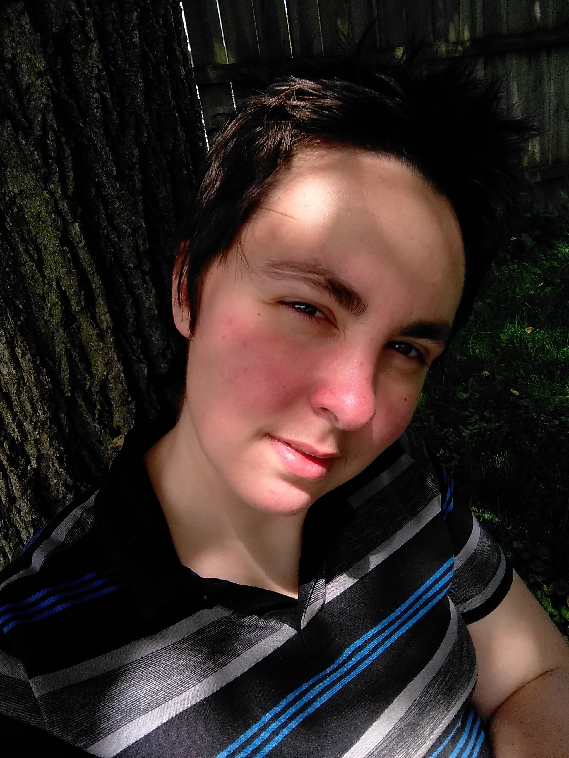 Photo of KJ, who has short brown hair, a striped shirt, and is smizing into the camera. They are a contributor to Best Lesbian Erotica Vol 5