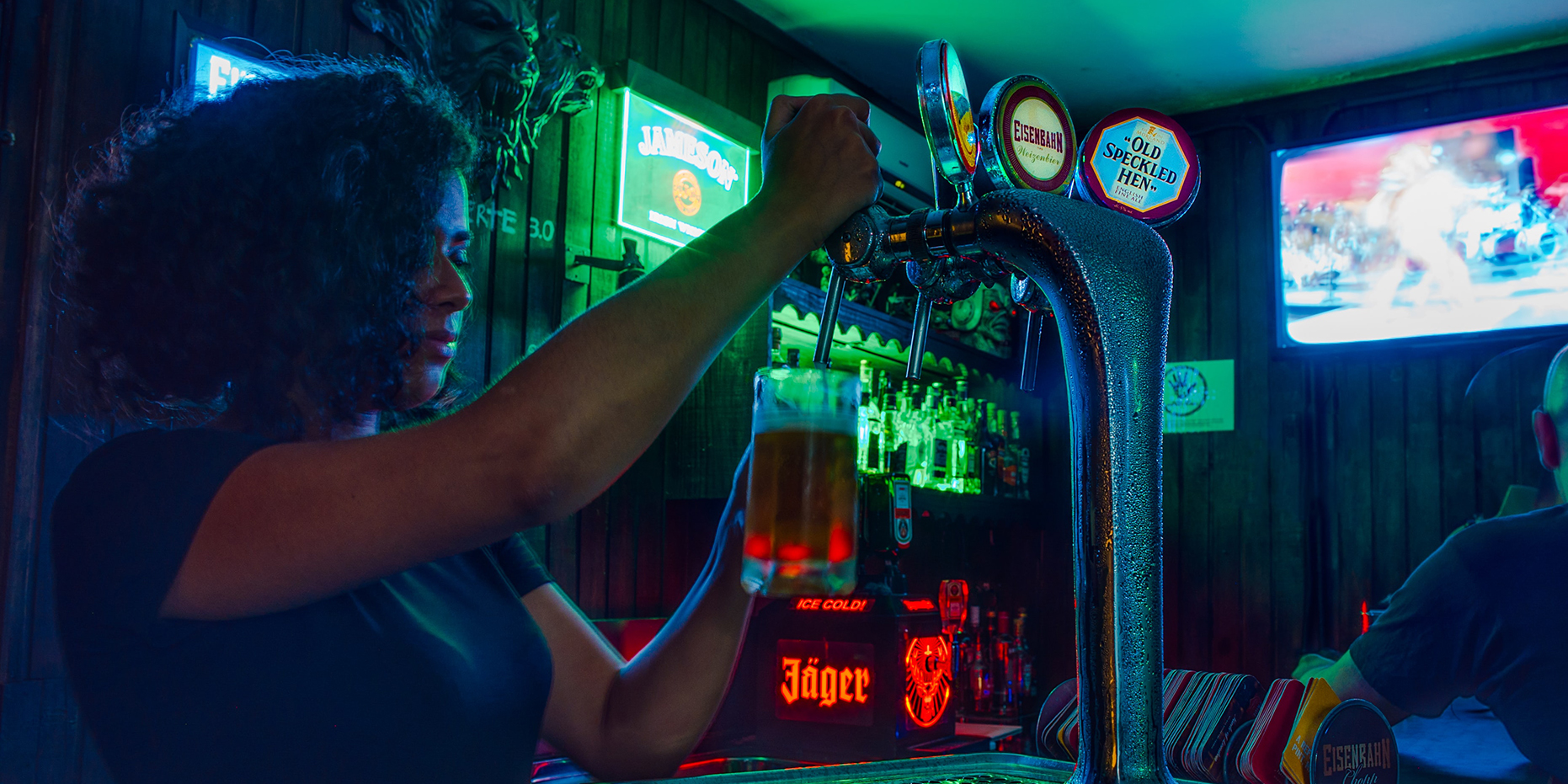 A woman with curly hair in a dark bar pours a draft from a spigot.