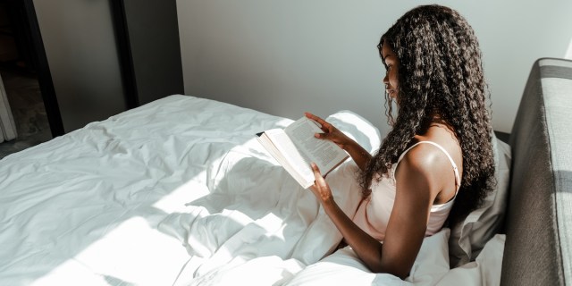 a Black person with long hair reading in bed
