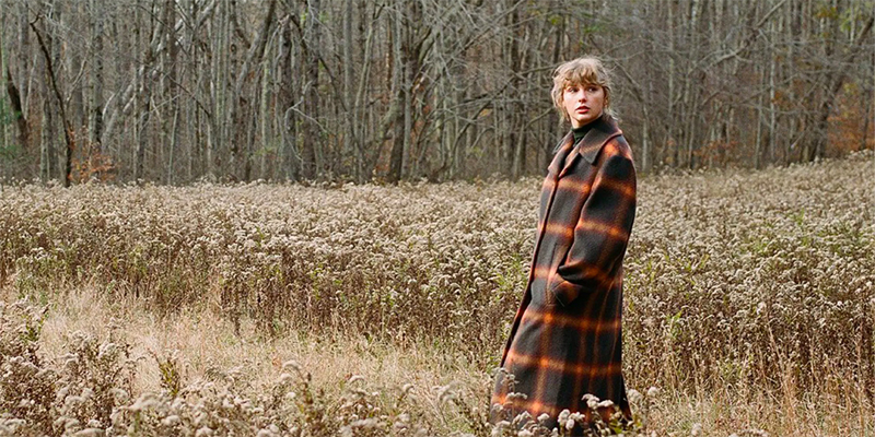 Taylor Swift stands in a field in a cottagecore-esque peacoat for Evermore.