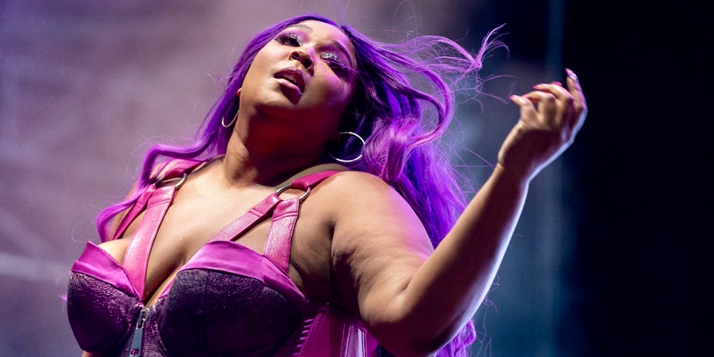 Lizzo in a purple wig is performing on stage in a hot pink bra.