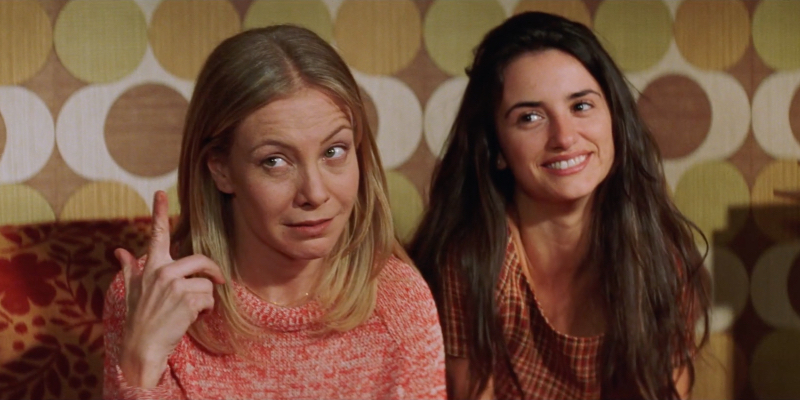 A still from the 35th best lesbian movie of all time All About My Mother.  A woman shapes her fingers to indicate someone being crazy while sitting next to a younger woman.