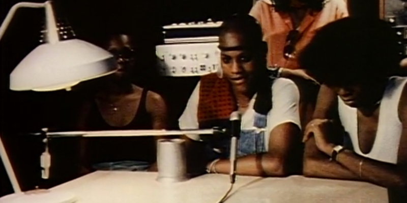 A still from Born in Flames. Four women sit around a radio microphone.